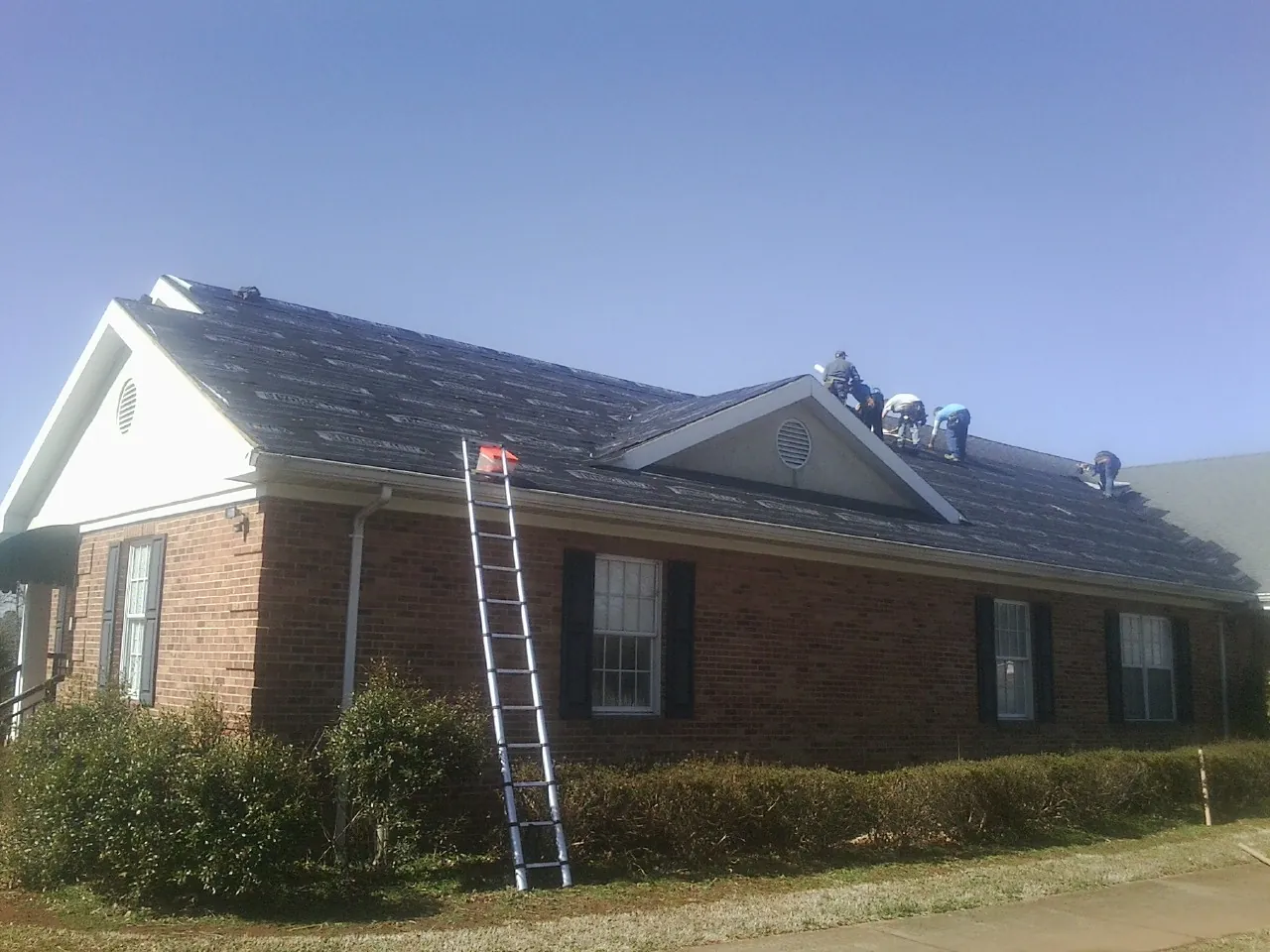 Crew tearing shingles off a brick ranch roof with a ladder set — Emergency Roof Repair work by our crew in Hillside