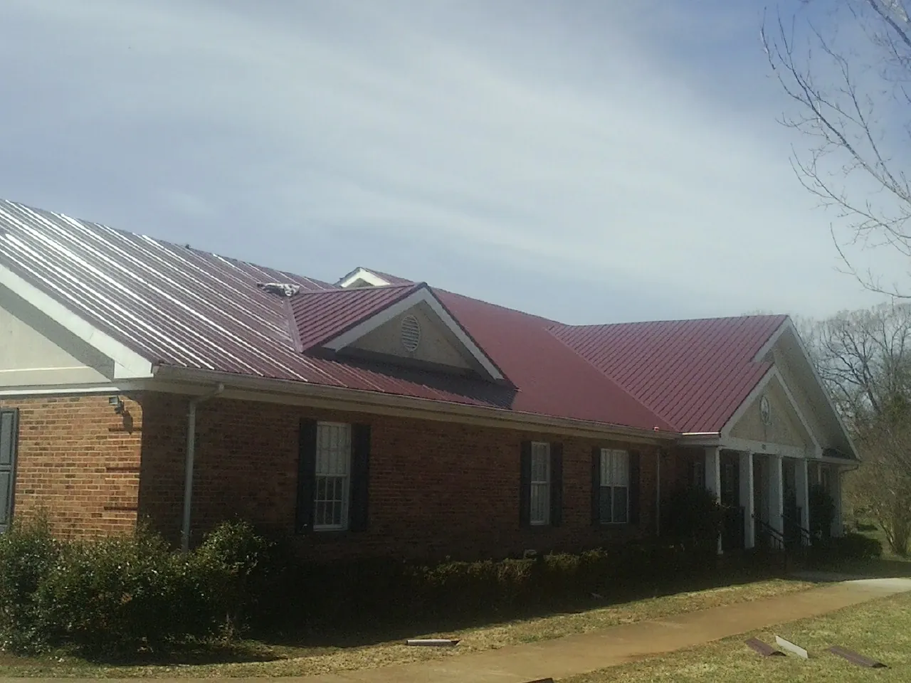 Red metal roof with gabled entries on a long brick building, from a Hail Damage Roof Repair job in Hillside