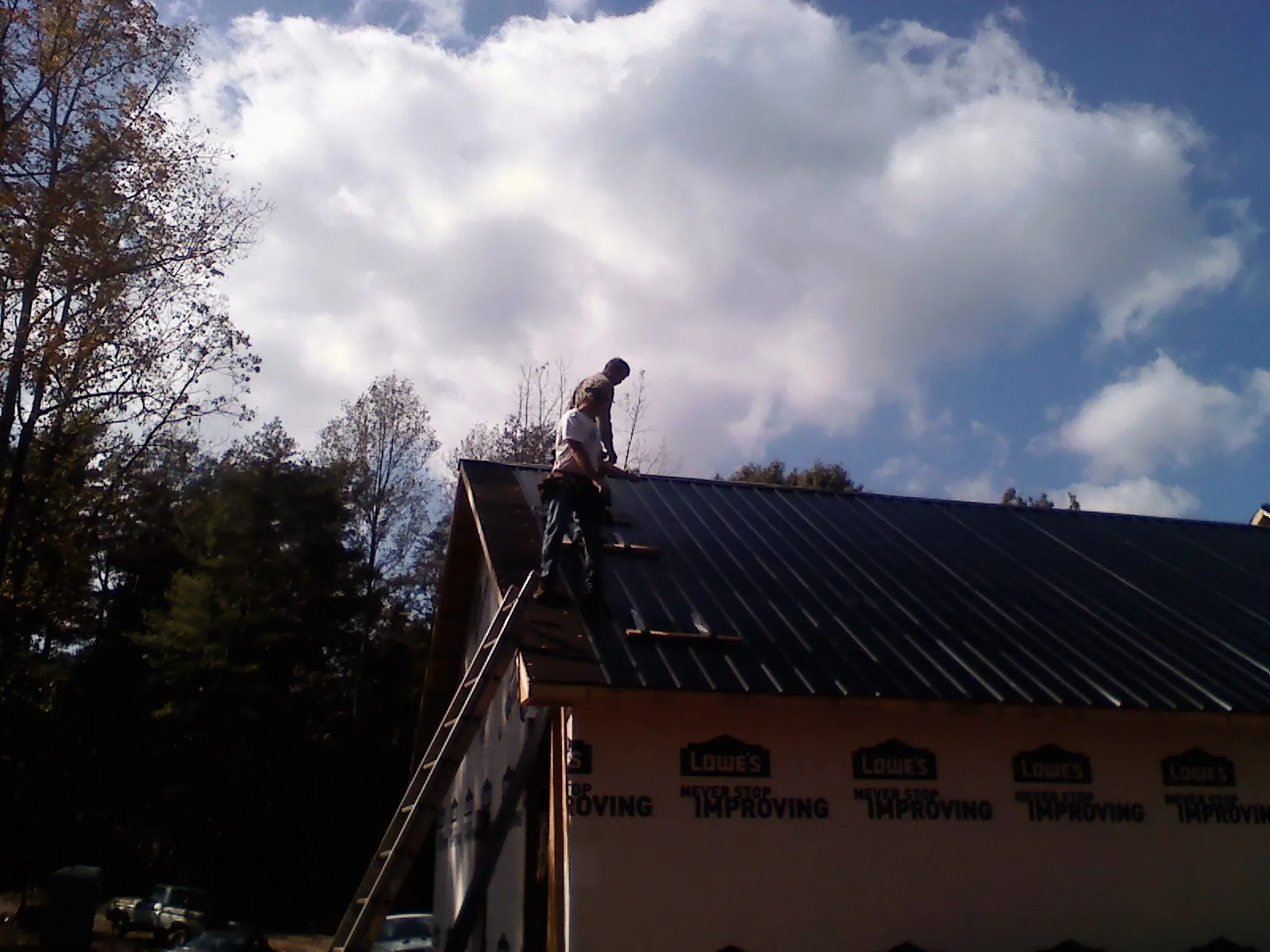 Roofer fastening dark metal panels high against a cloudy sky, from a Roof Inspection job in Hillside